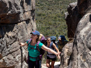 Three people, touching rocks and climbing the Grampians Trails on a sunny day